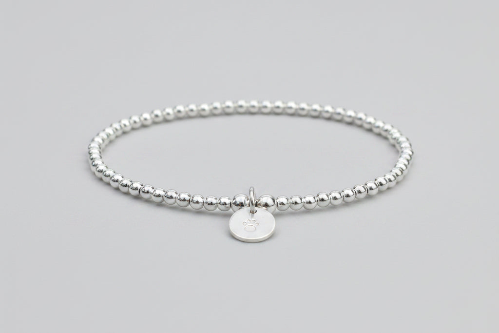 A sterling silver dog pawprint stretch bracelet with silver plated beads, featuring a hand stamped paw print disc.
