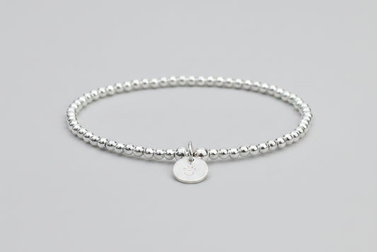 A sterling silver dog pawprint stretch bracelet with silver plated beads, featuring a hand stamped paw print disc.