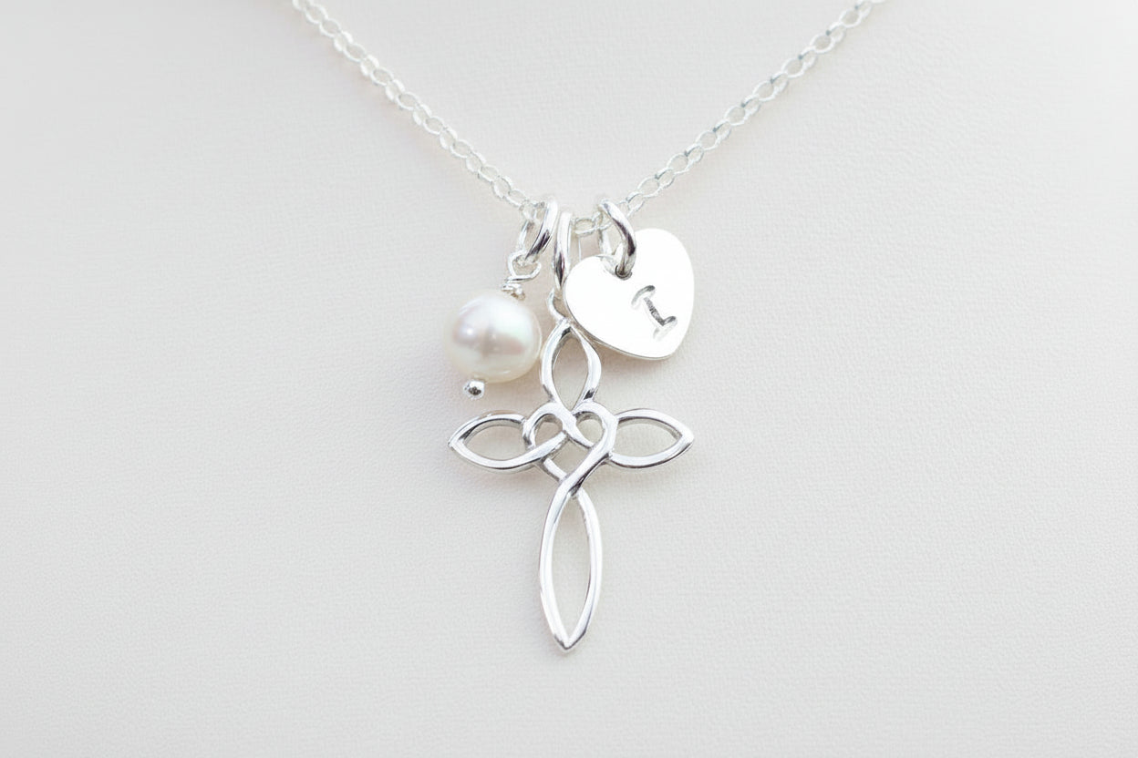 A silver cross necklace with a freshwater pearl and a personalized heart tag initial charm.