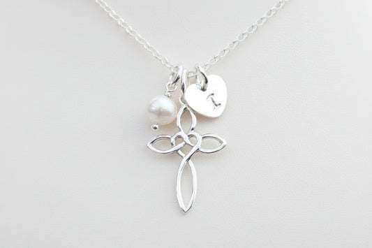 A silver cross necklace with a freshwater pearl and a personalized heart tag initial charm.