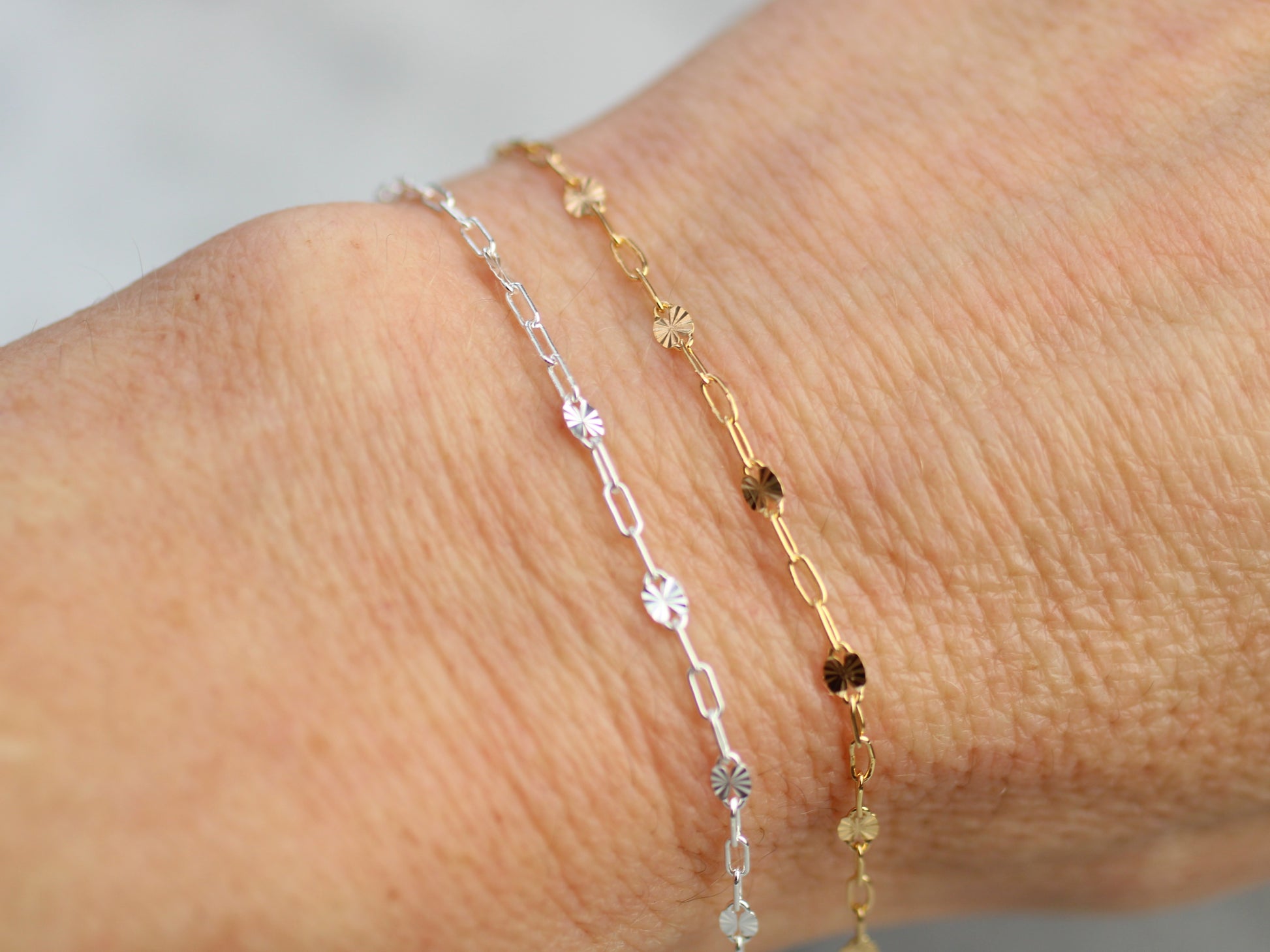 Two gold and silver bracelets on a wrist against a neutral background