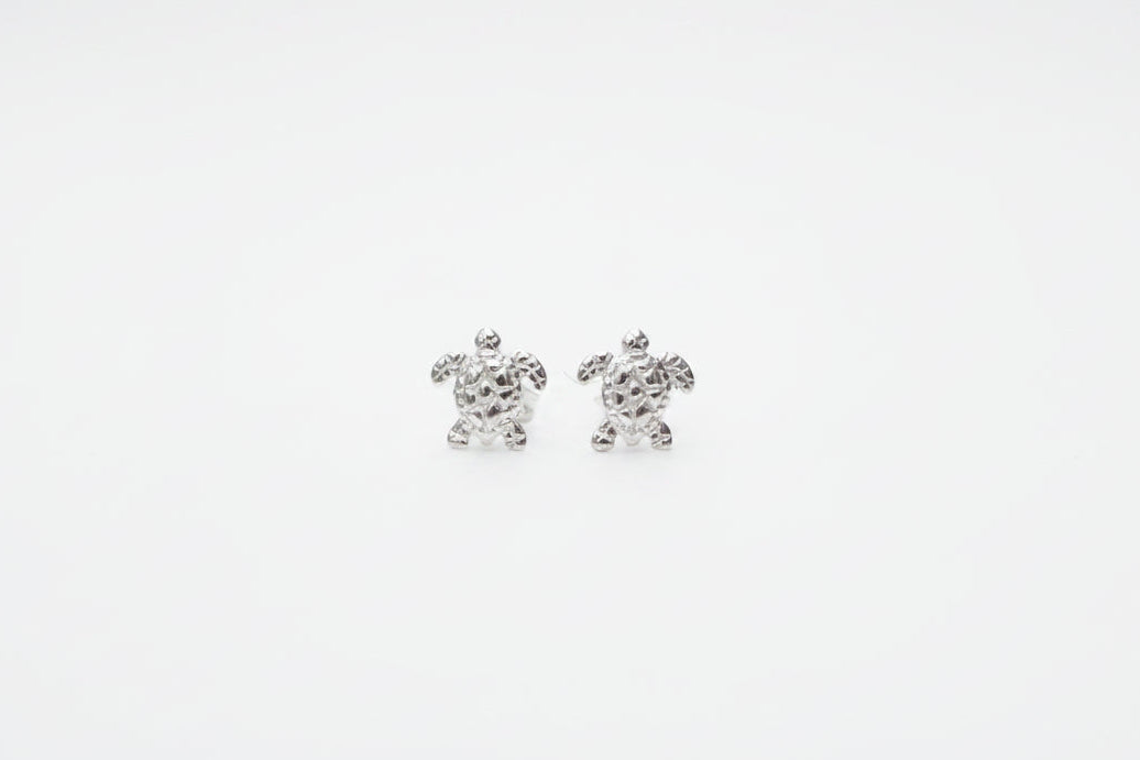 Silver turtle earrings on a marble surface with a soft fabric background