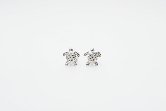 Silver turtle earrings on a marble surface with a soft fabric background