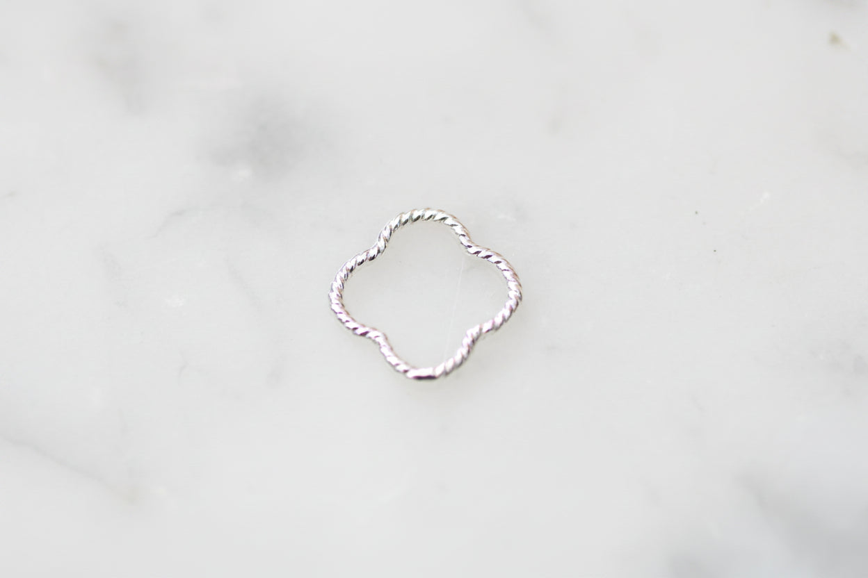 A delicate silver ring with a twisted, rope-like texture and an open quatrefoil or clover-like shape, resting on a light gray marble surface.