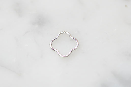 A delicate silver ring with a twisted, rope-like texture and an open quatrefoil or clover-like shape, resting on a light gray marble surface.