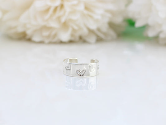 A silver heart-shaped ear cuff placed on a white surface, with a blurred background of flowers.