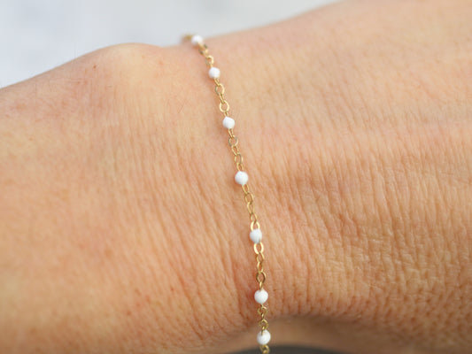 Gold bracelet with white beads on a wrist against a neutral background
