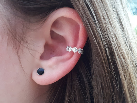 A person wearing a sterling silver metal ear cuff with a floral pattern design, with the cuff visible through the ear.